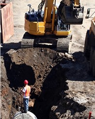 Man in workwear down a hole in the ground with a digger in the background to test for TPH in Soil at Remediation